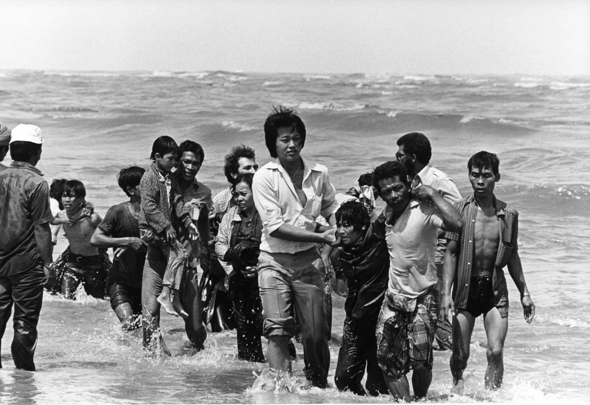 A black and white photo of Vietnamese refugees disembarking from a boat and walking in the ocean