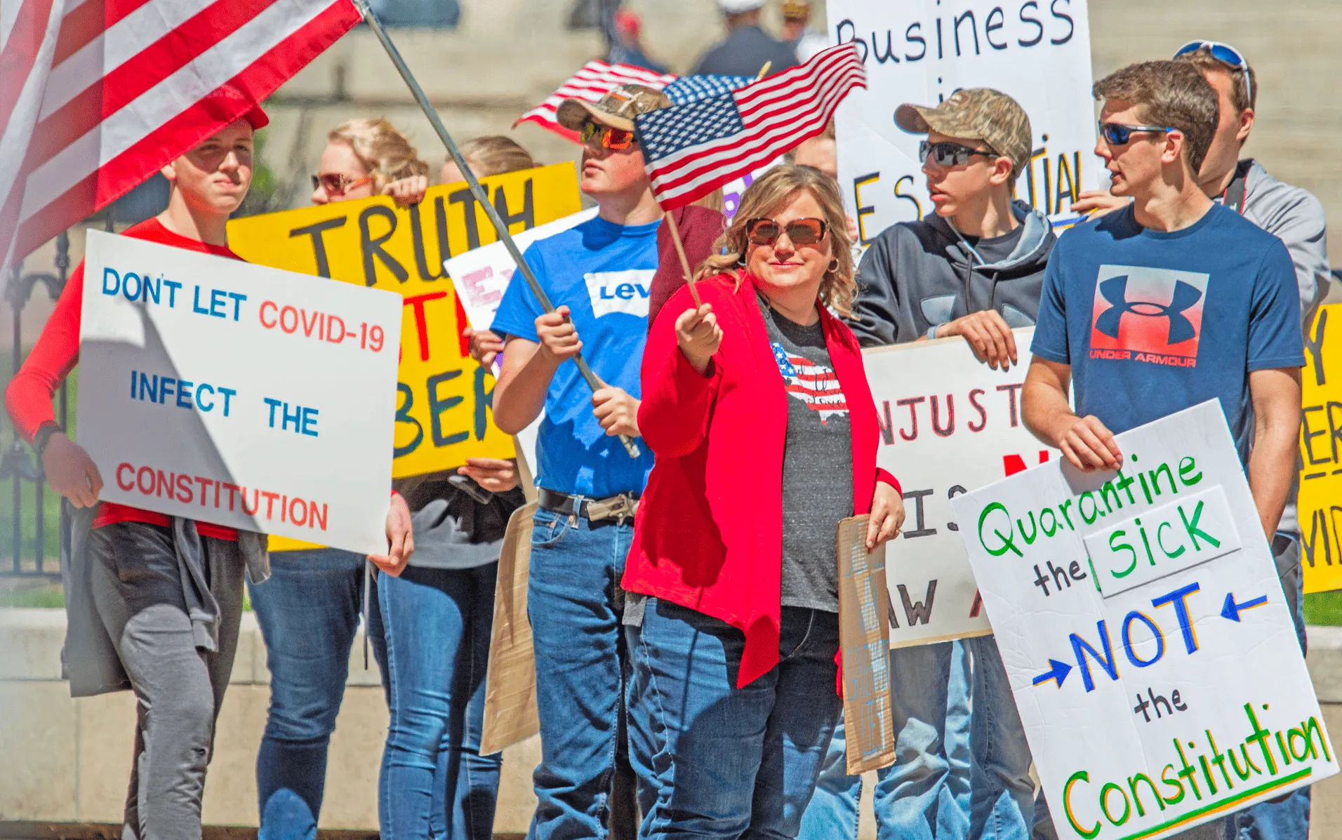 Photo of a protest regarding the government's response to Covid-19, including posters that say "Quarantine the Sick, Not the Constitution" and "Don't let Covid-19 Infect the Constitution"